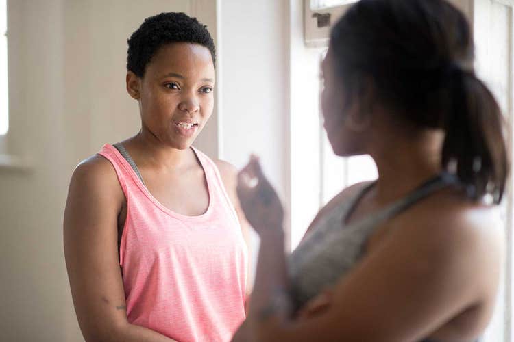 Up-close shot of two women in workout wear talking near window
