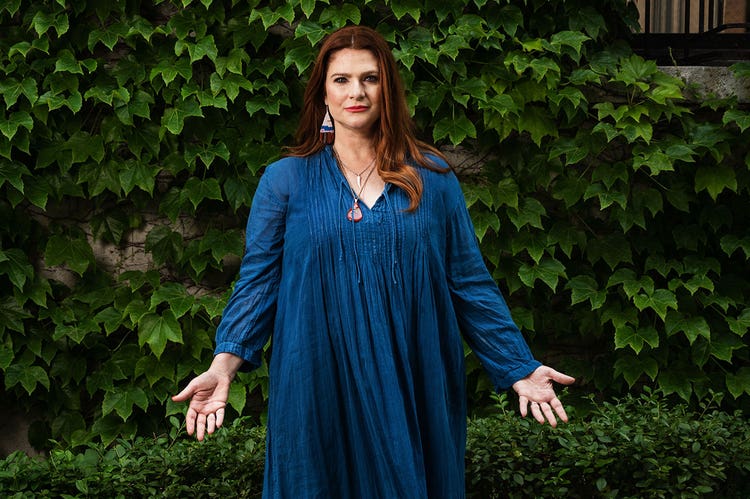 Elana Kilkenny stands with outstretched hands in front of a wall of ivy