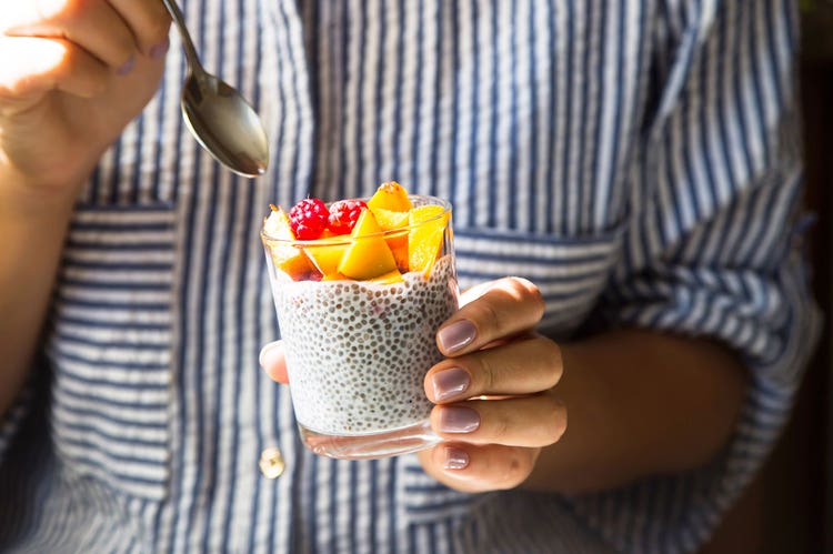 Closeup of hands holding a spoon and a glass of chia seed pudding with cut fruit