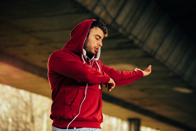 Man in hoodie stretching arms under the bridge