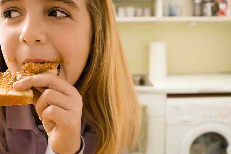 Closeup of a child happily eating a piece of toast with nut butter