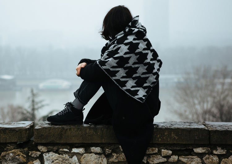 Girl sitting on wall wrapped in checked blanket or shawl