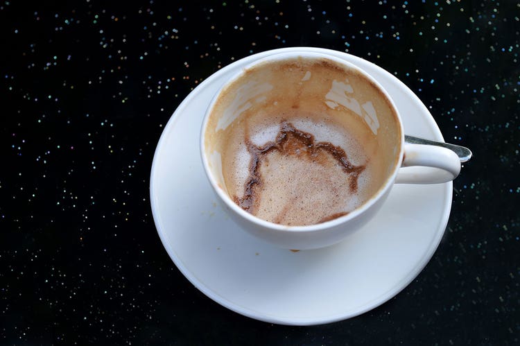 An empty white latte mug with dregs of espresso on a black counter