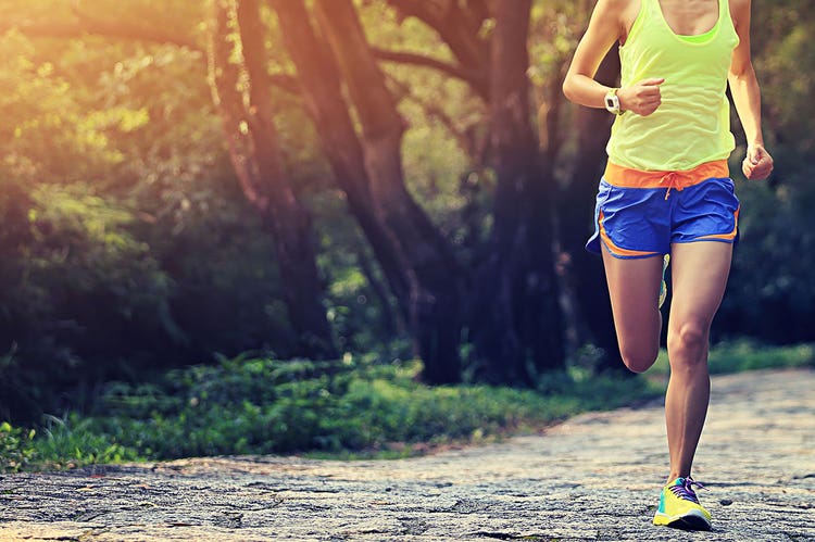 A person runs towards the viewer on a nature trail with trees and grass