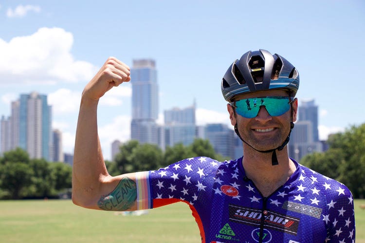 Phil Gaimon standing with one arm flexed while wearing his biking gear